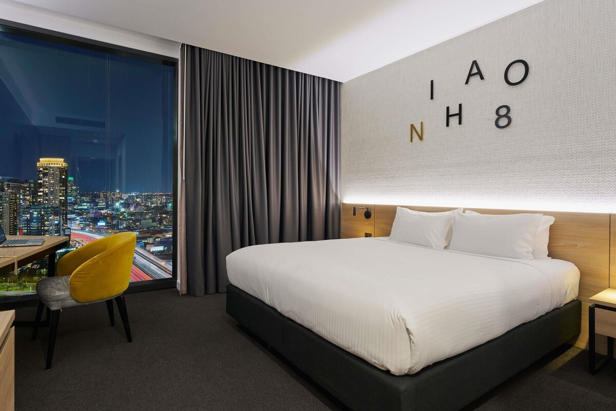 Une chambre d’hôtel avec un grand lit, un bureau avec une chaise et une vue sur le paysage urbain.