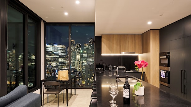 A modern kitchen with a city view, a dining area with a sofa and chairs, and a bar area with a wine bottle and glass.