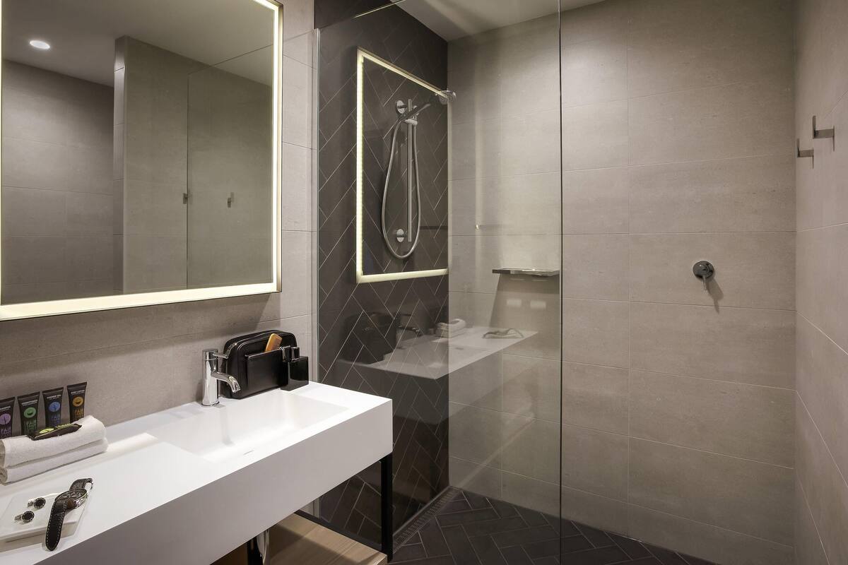 A modern bathroom with a glass-enclosed shower, a white sink with toiletries, and a large mirror.