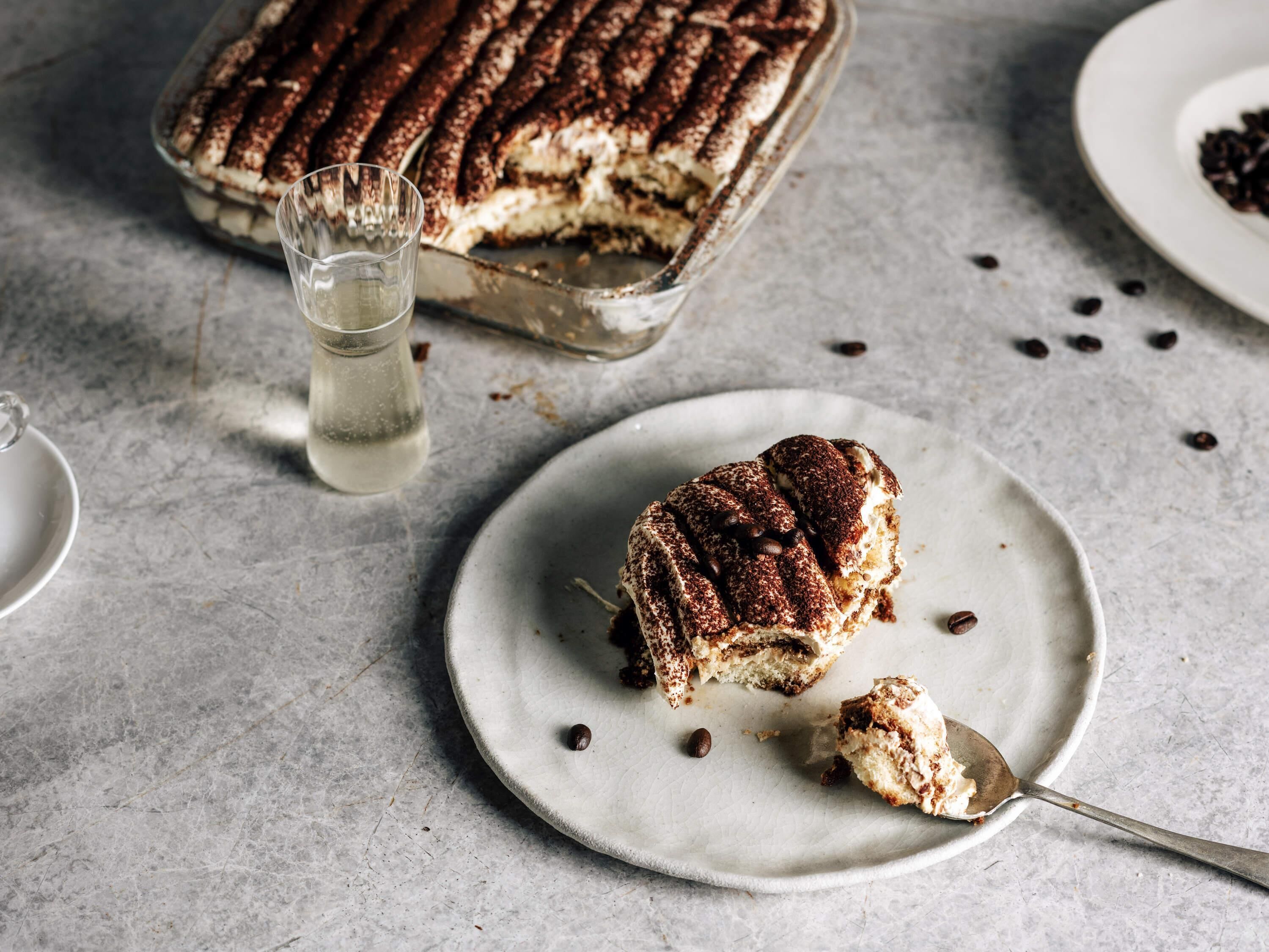Ett fat med desserter, med en tårtbit på en tallrik, ett glas vatten och några kaffebönor utspridda.