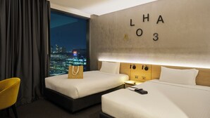 A hotel room with two beds, a view of the city at night, a large wall with letters, and a yellow chair. - Novotel Melbourne South Wharf (South Wharf)