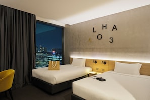 A hotel room with two beds, a view of the city at night, a large wall with letters, and a yellow chair. - Novotel Melbourne South Wharf (South Wharf)