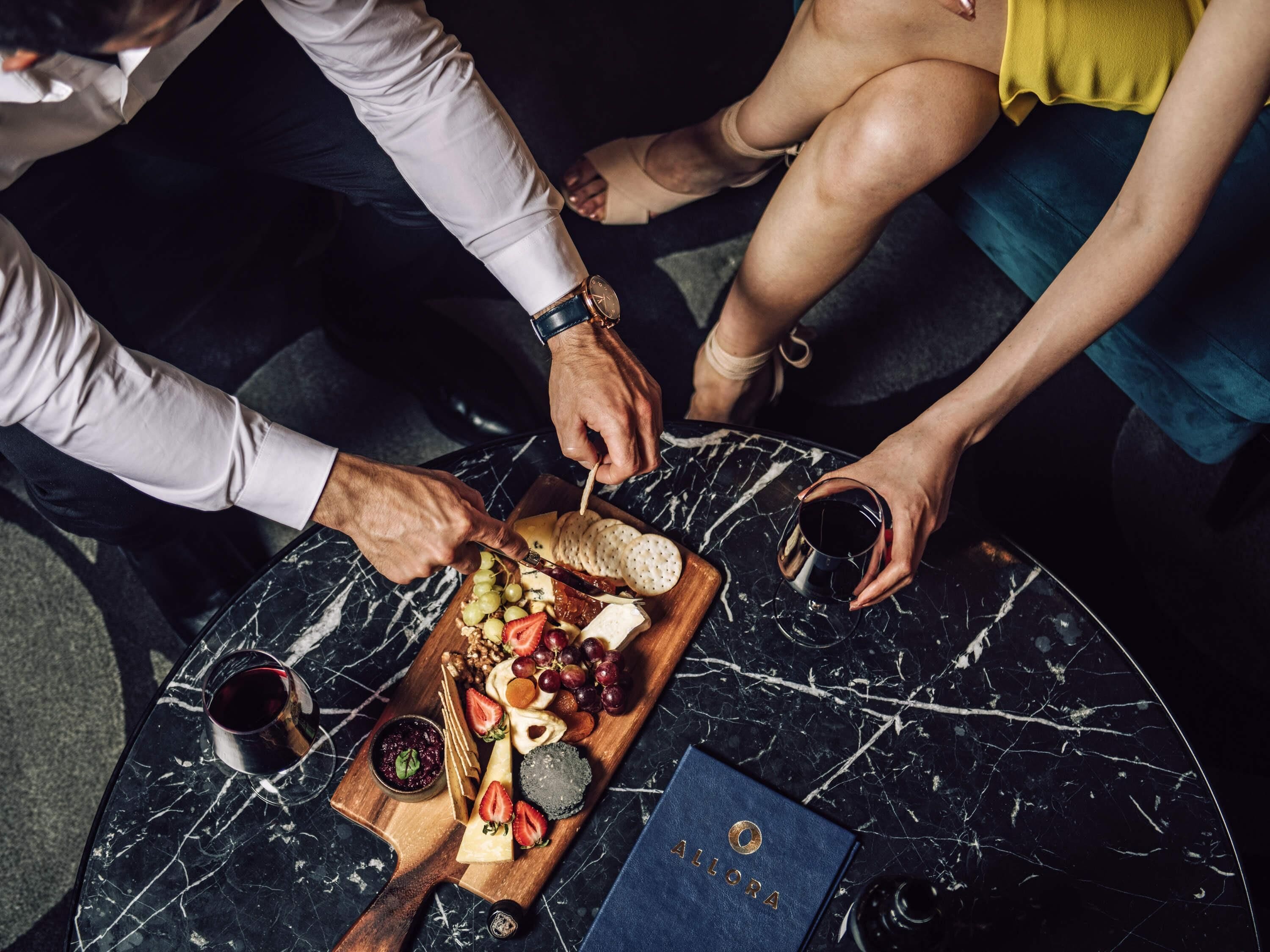 A marble table with a charcuterie board, a bottle of wine, and a blue booklet.