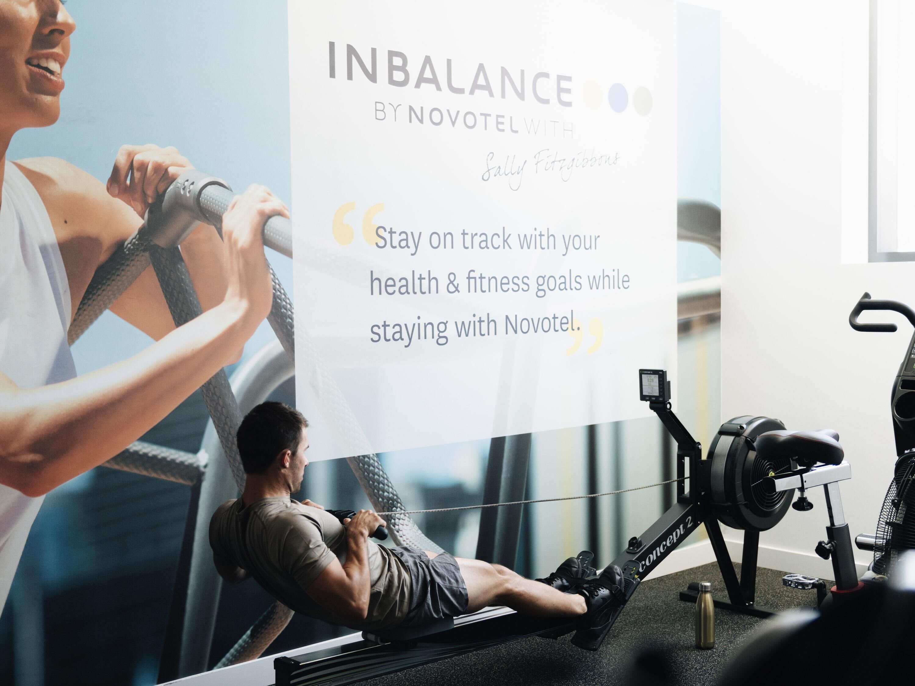 A gym with exercise equipment, a poster with a quote, and a person using a rowing machine.