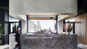 A modern bar area with a marble countertop, a city view, and a large cylindrical light fixture.