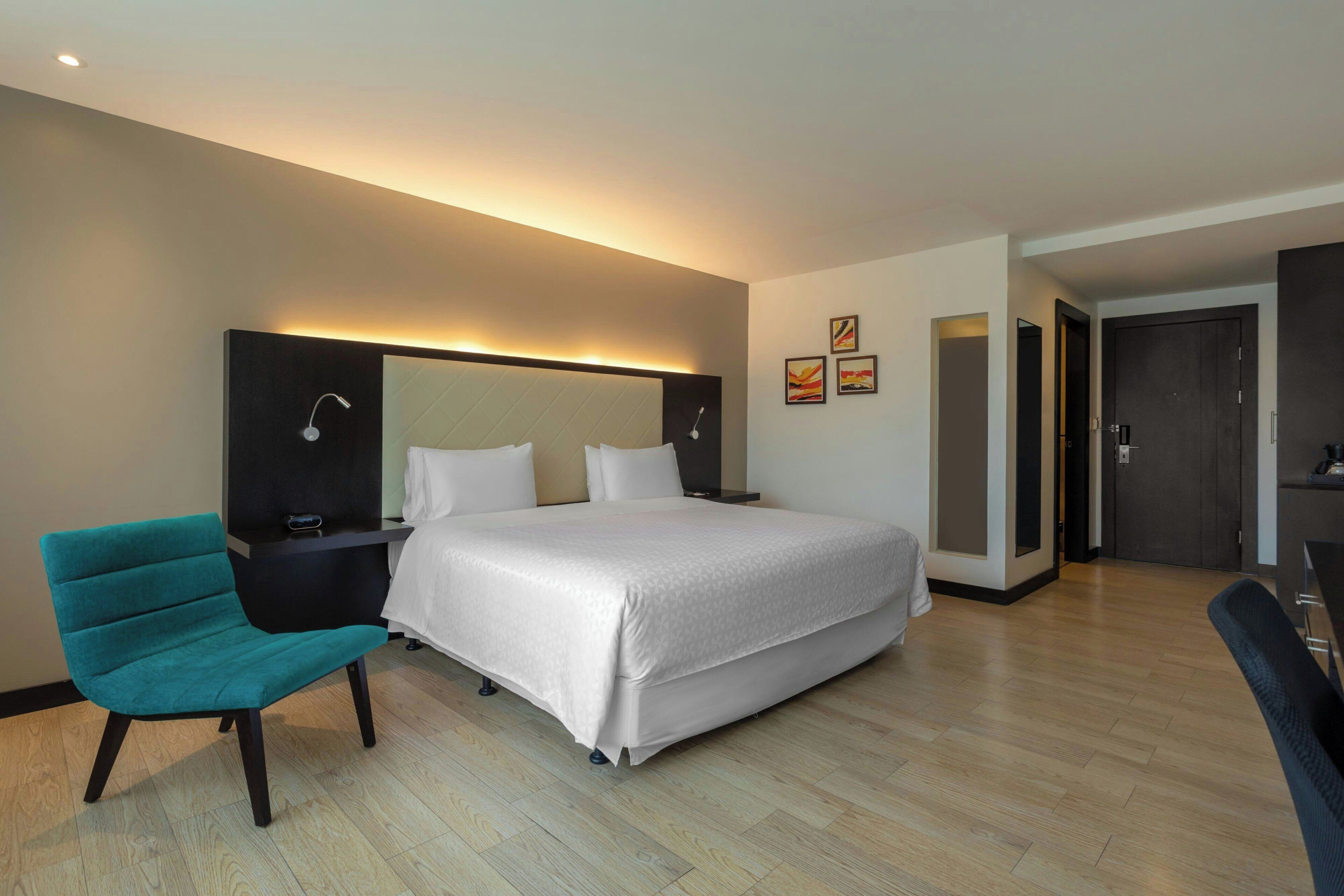 Una habitación de hotel moderna con una cama, una silla, un escritorio y una puerta.