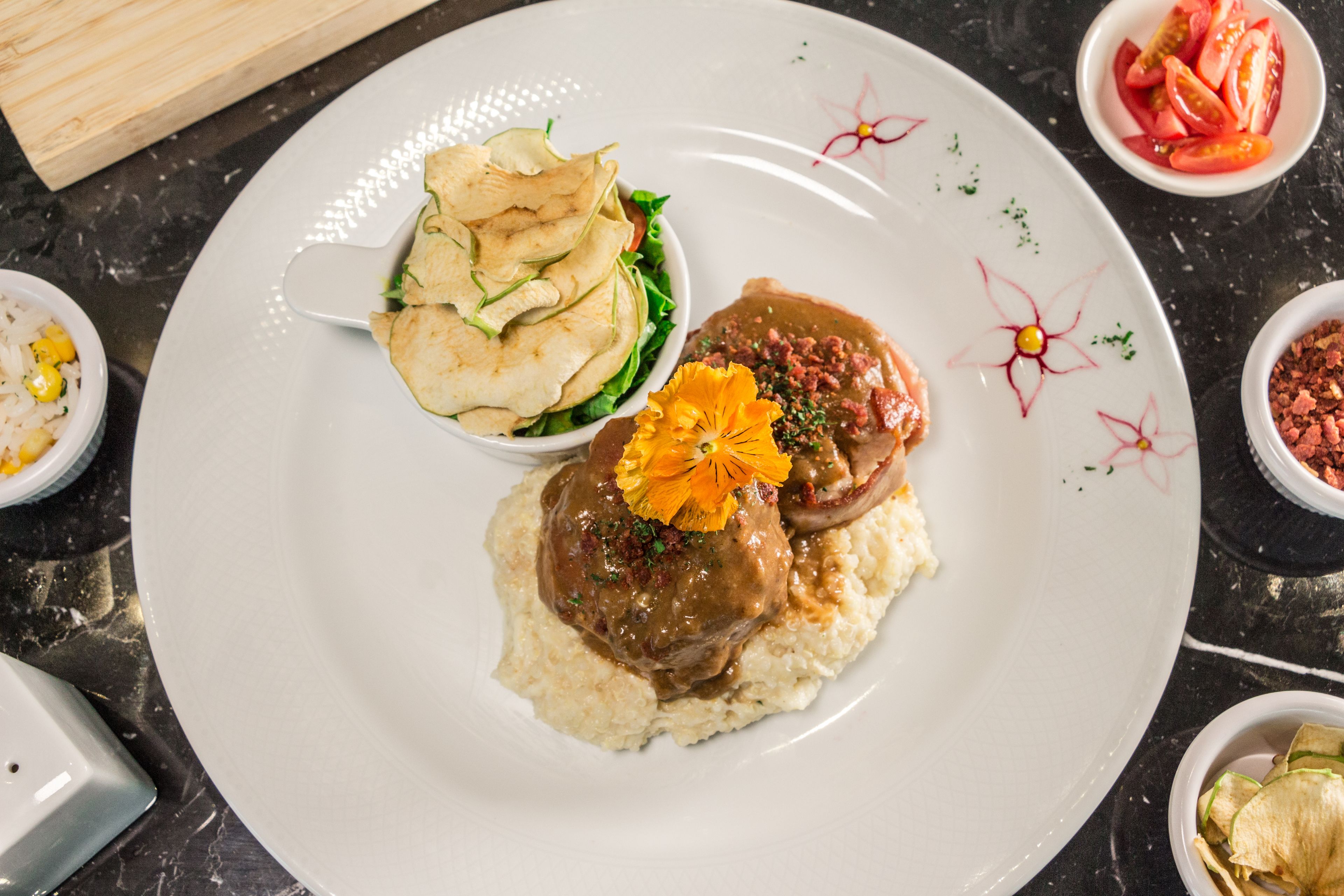 A plate with a meat dish, a side of chips, and a small bowl of sliced tomatoes.