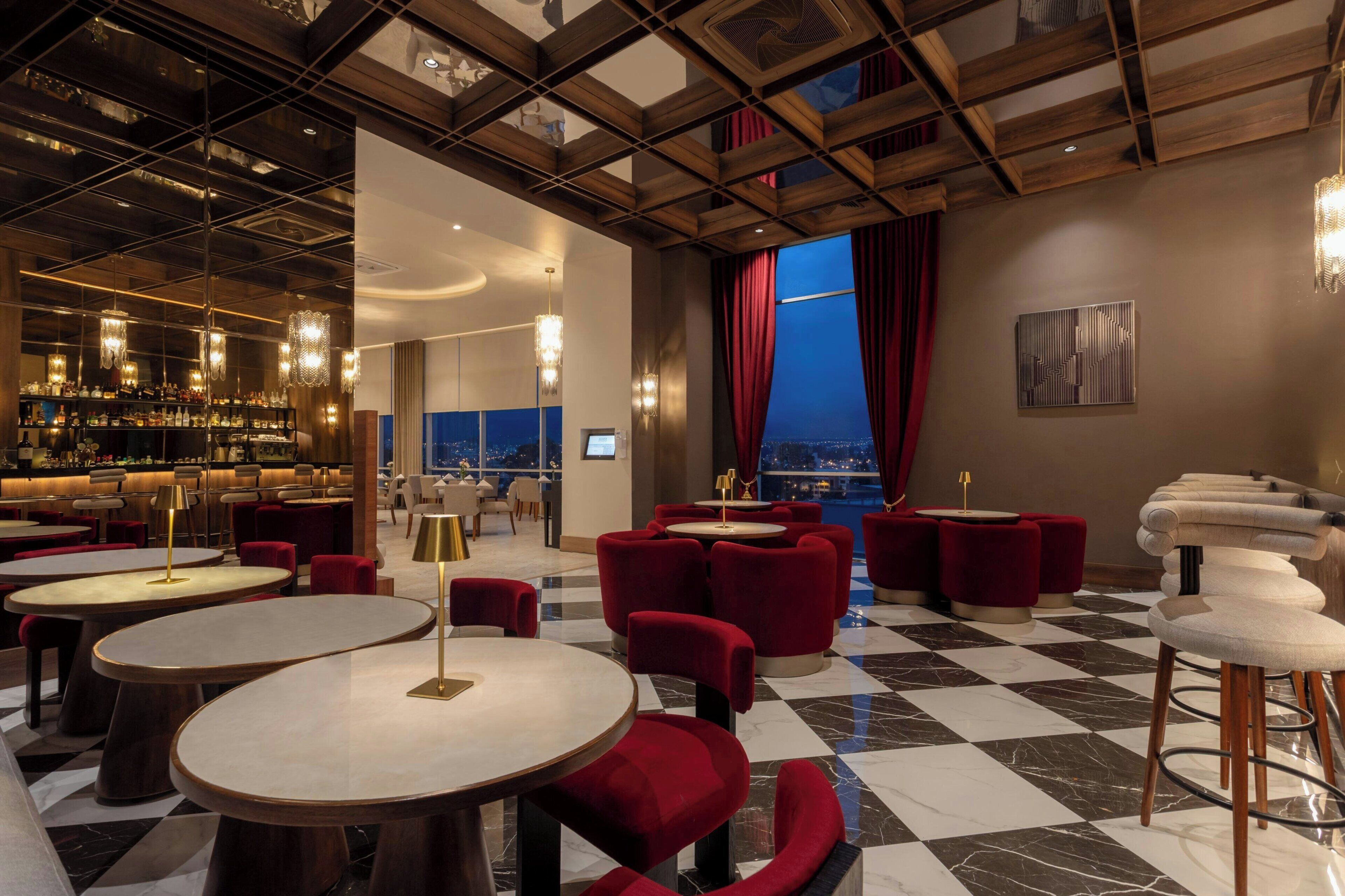 A modern bar area with round tables, red upholstered chairs, and a checkered floor.