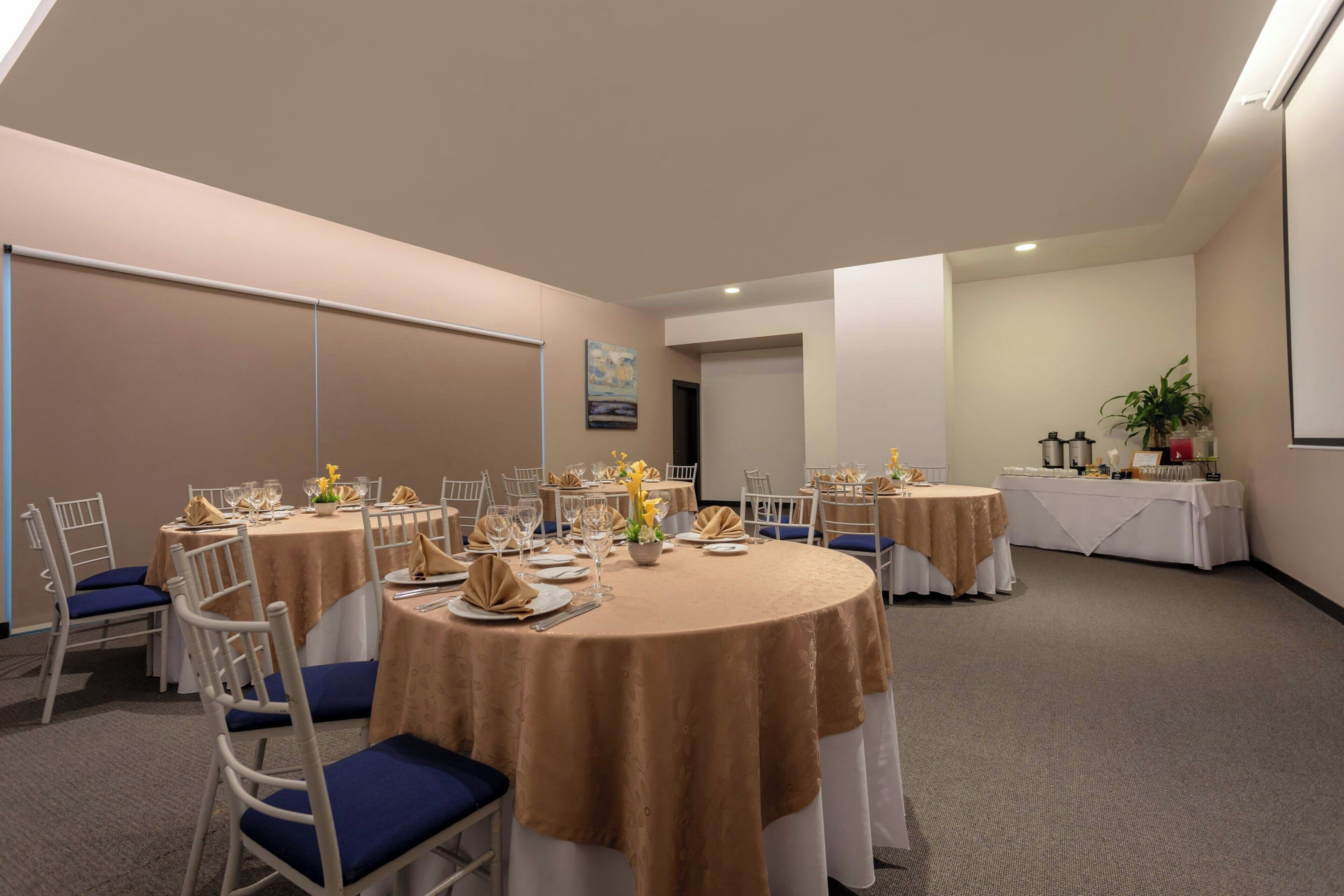 A conference room with round tables, white chairs, and beige tablecloths.