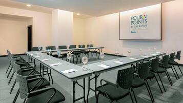 Un salón de conferencias con una mesa larga, varias sillas y una pantalla proyectora que muestra “FOUR POINTS BY SHERATON Cuenca”.