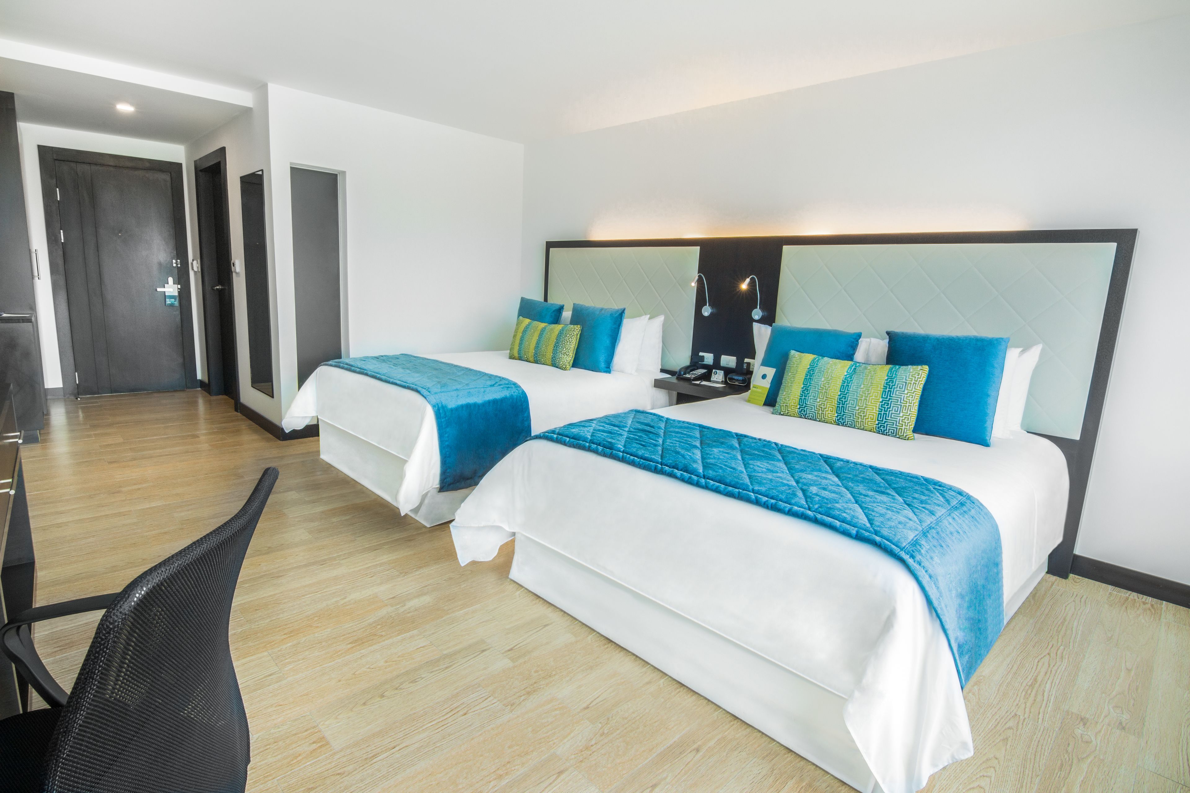A hotel room with two beds, each with blue and white bedding, a desk, and a chair.