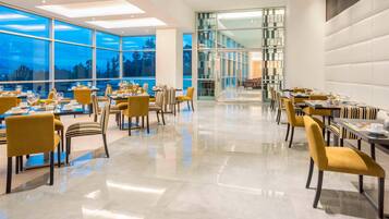 A modern dining area with tables set for meals, large windows, and a high ceiling.