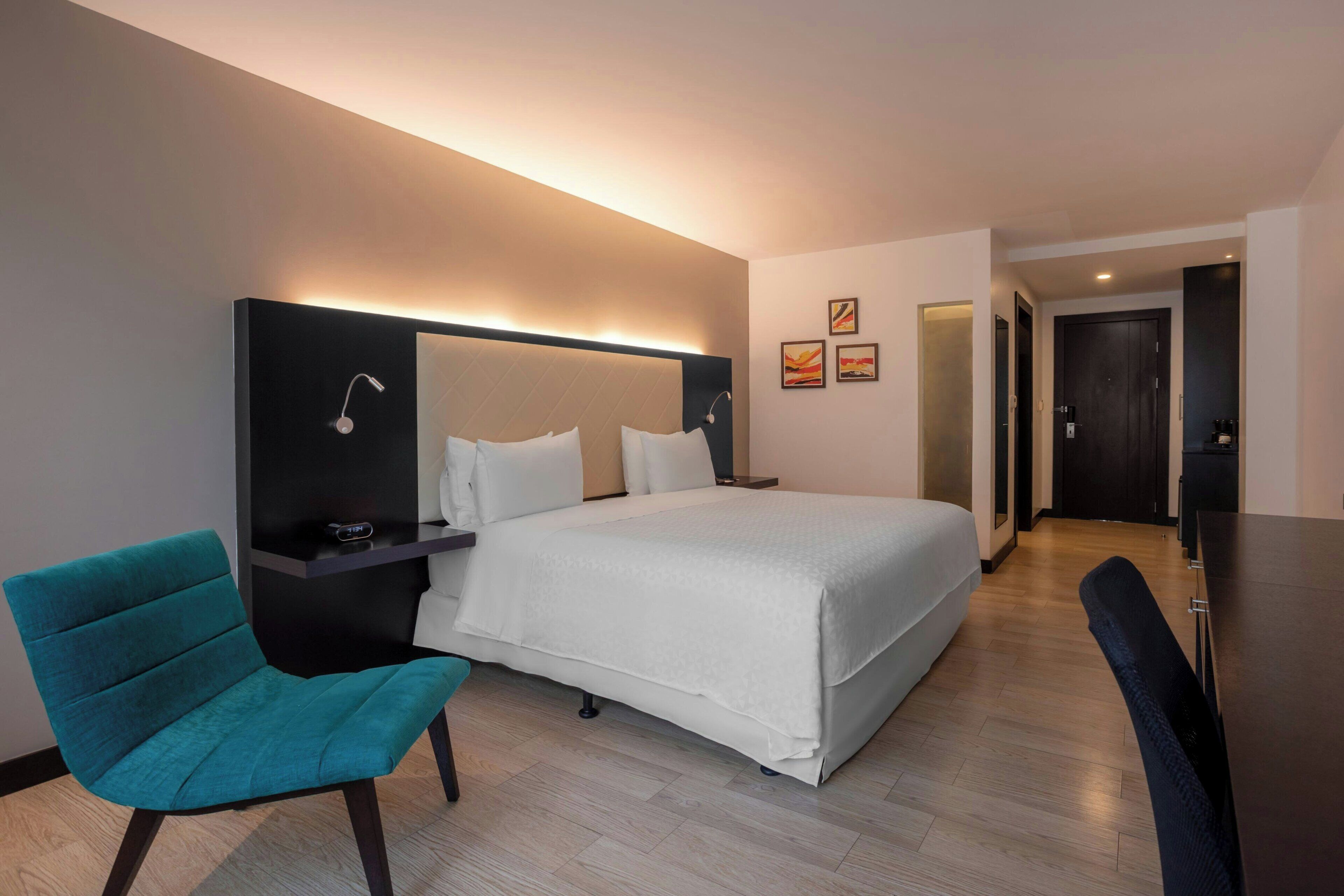 Una habitación de hotel con cama, escritorio, silla y mesita de noche.