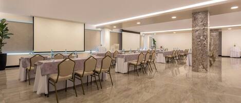 A spacious conference room with multiple tables and chairs, a large screen, and a marble pillar.