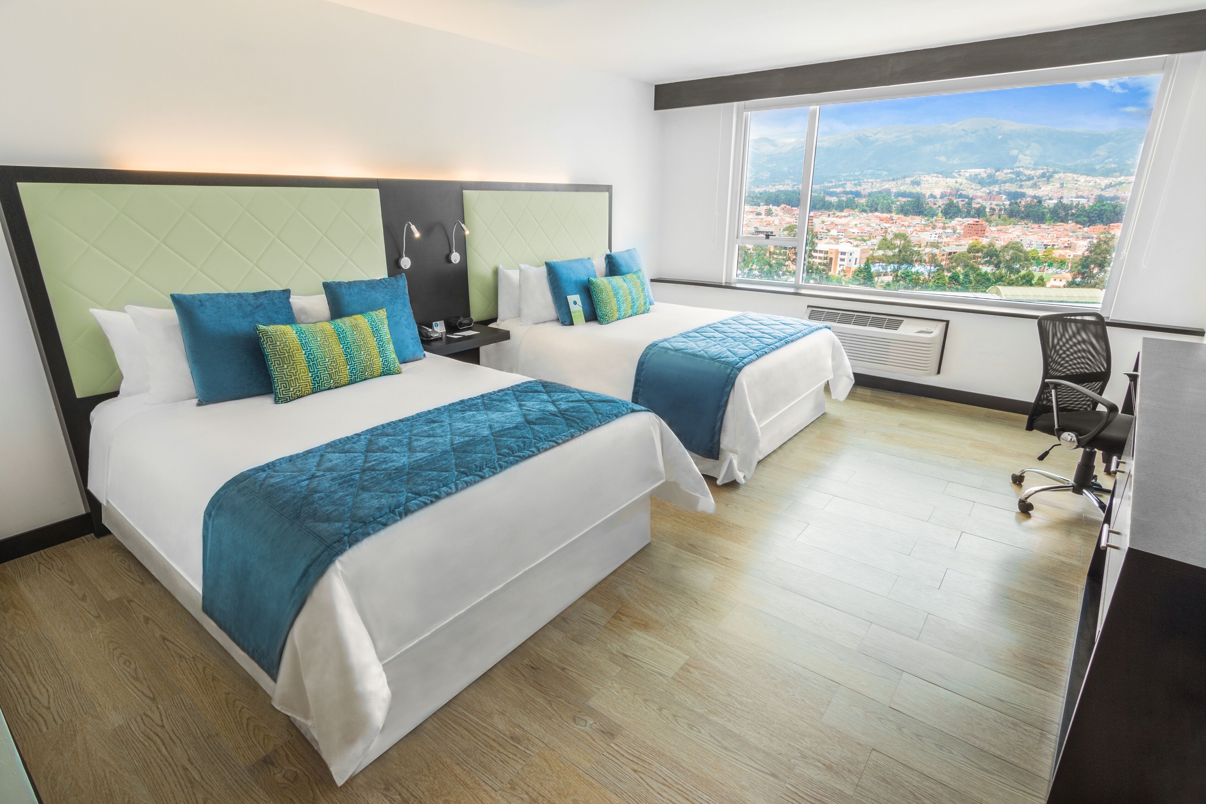 A hotel room with two beds, a large window with a city view, and a desk with a chair.