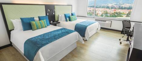 A hotel room with two beds, a large window with a city view, and a desk with a chair.