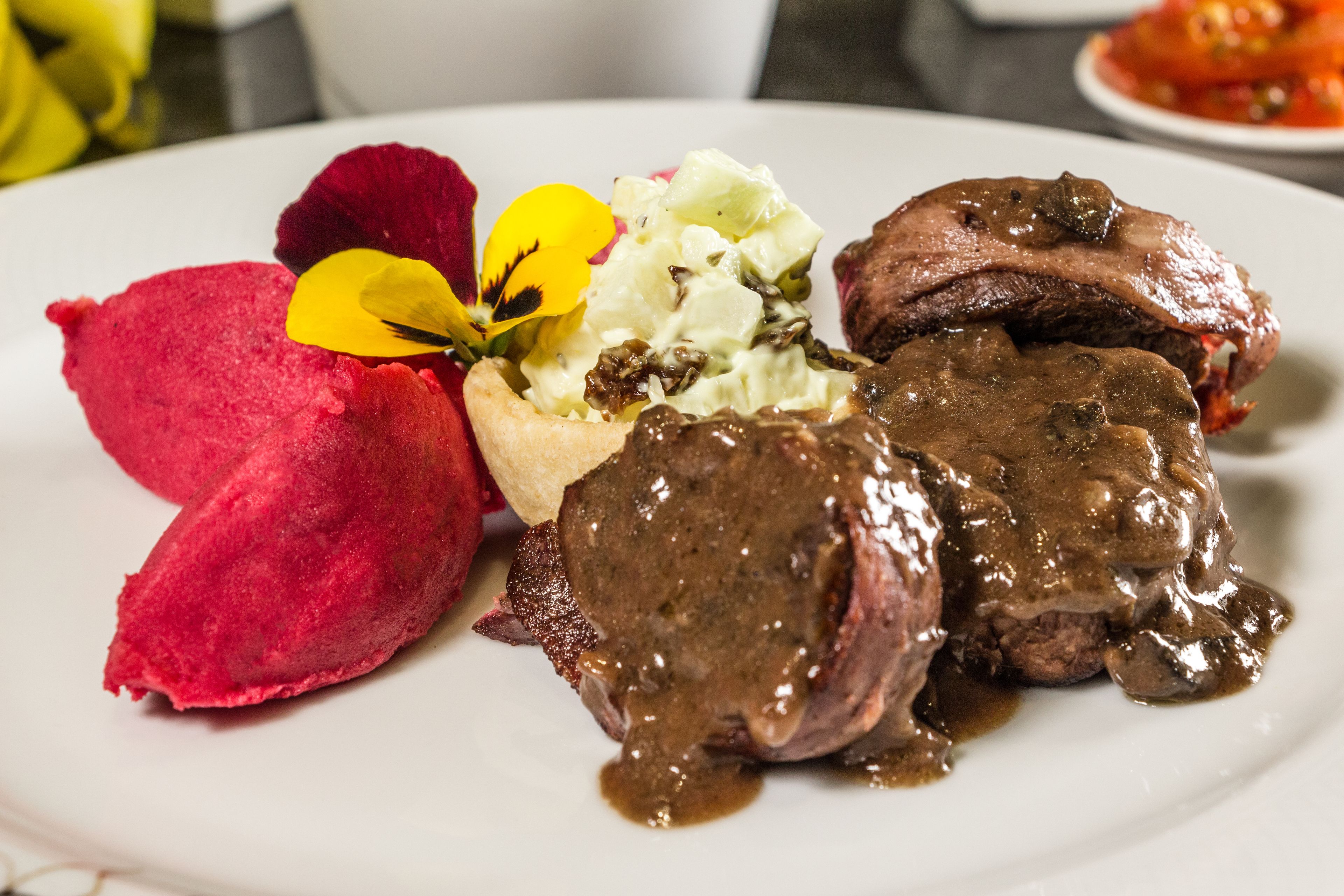 Un plato con un guiso de carne, una verdura roja y una flor amarilla.