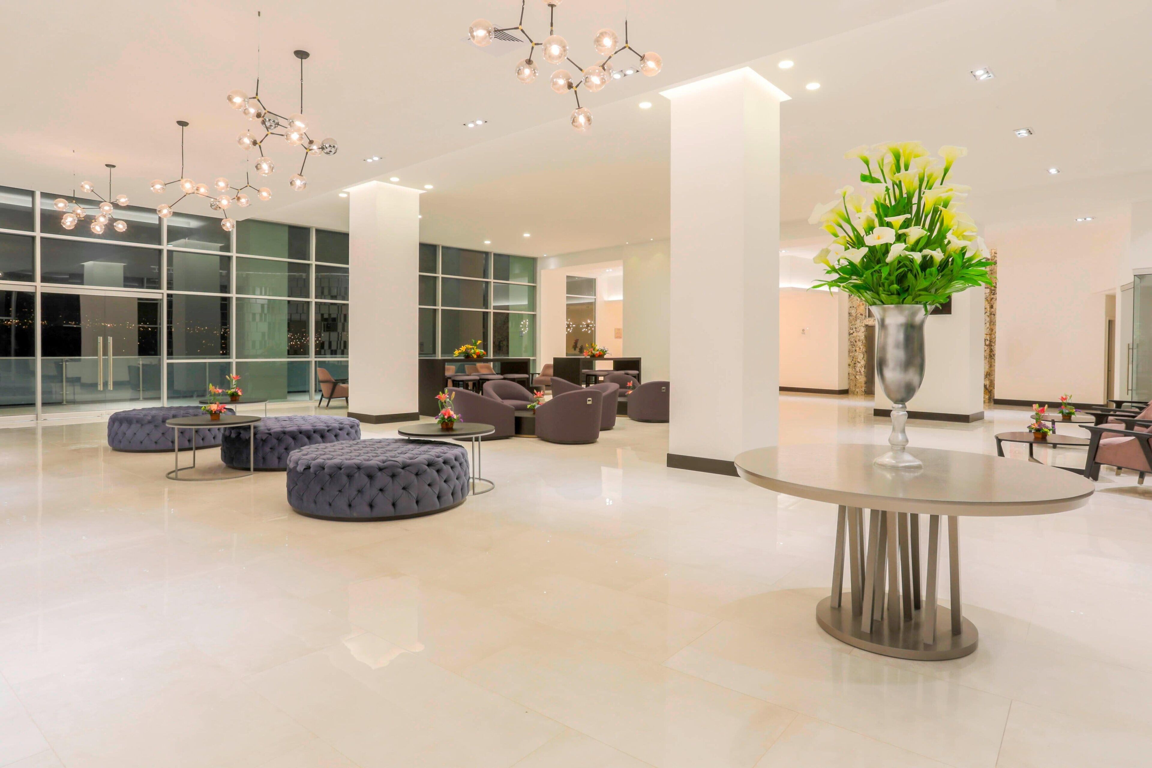 A spacious lobby with modern seating, a central round table, and decorative lighting.