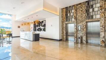 A modern lobby with a reception desk, a fireplace, and elevators.