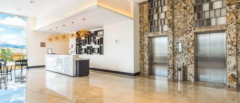 A modern lobby with a reception desk, a fireplace, and elevators.