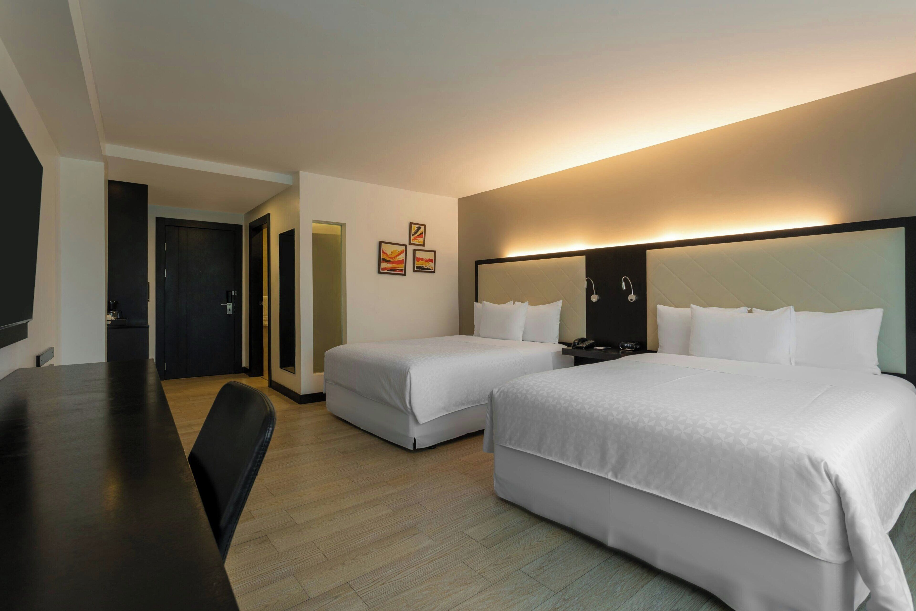 Una habitación de hotel con dos camas, un escritorio, una silla y un televisor.
