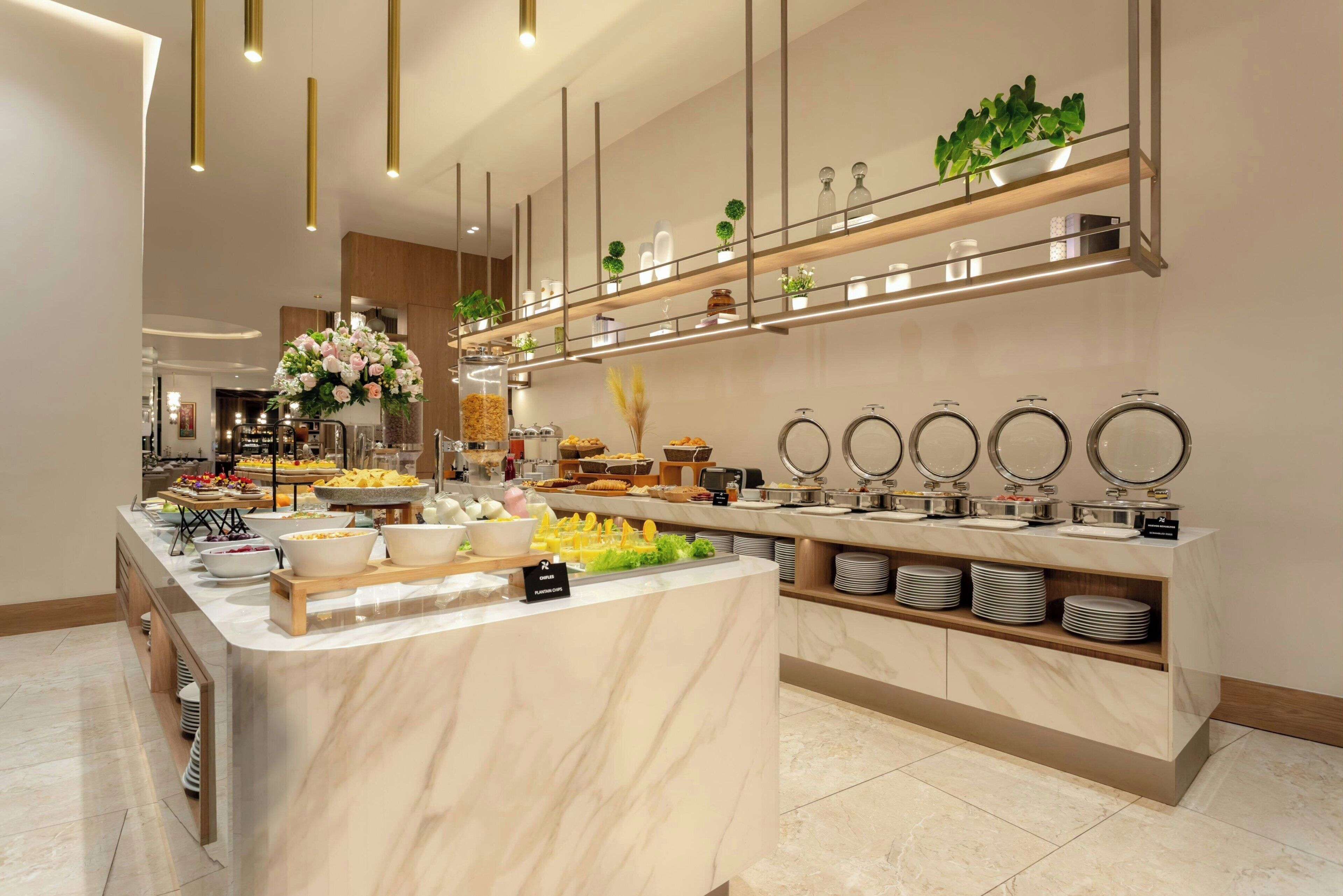 Disposição de buffet com diversos alimentos, um balcão de mármore e prateleiras com objetos decorativos.
