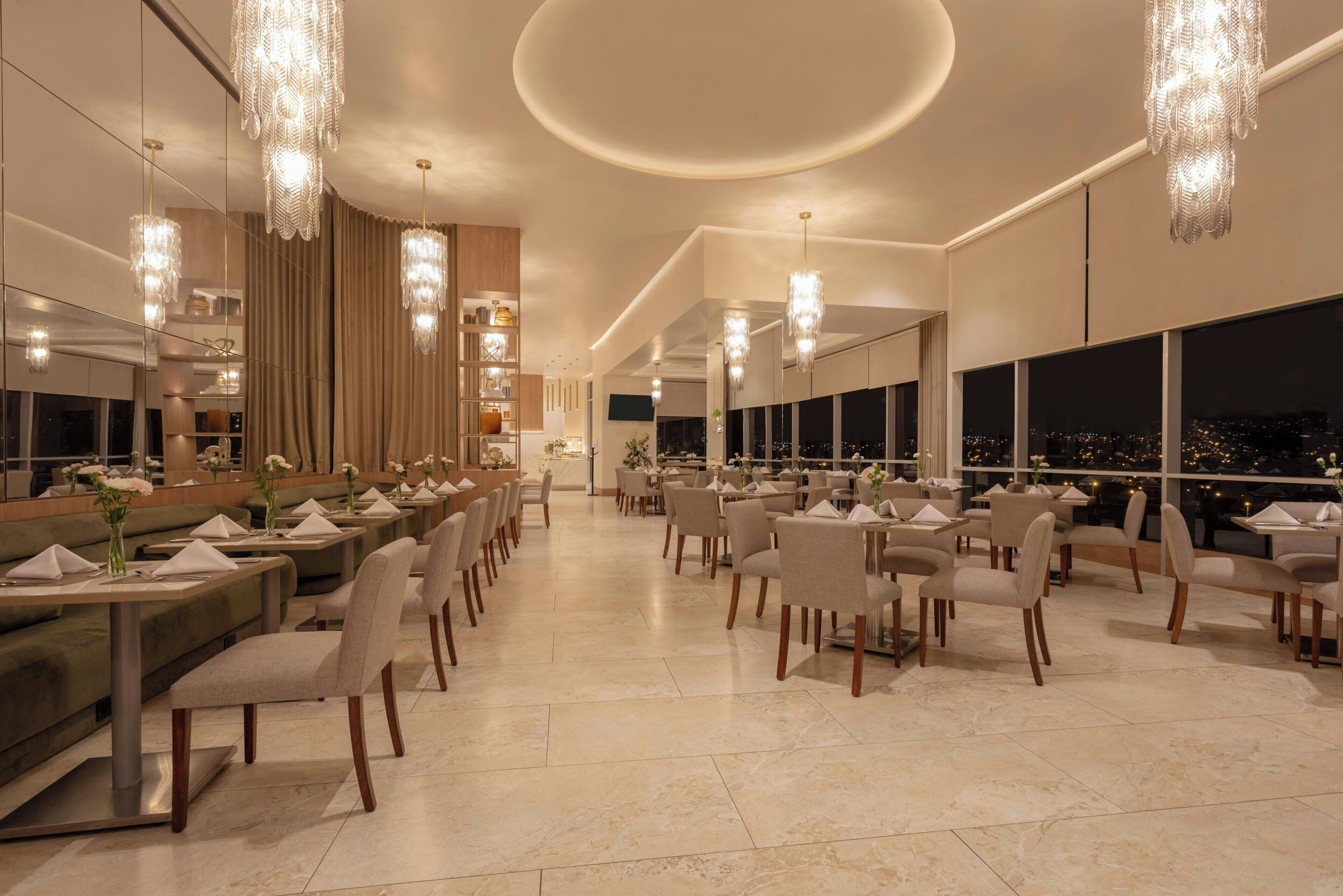 A modern restaurant with high ceilings, chandeliers, and a city view.