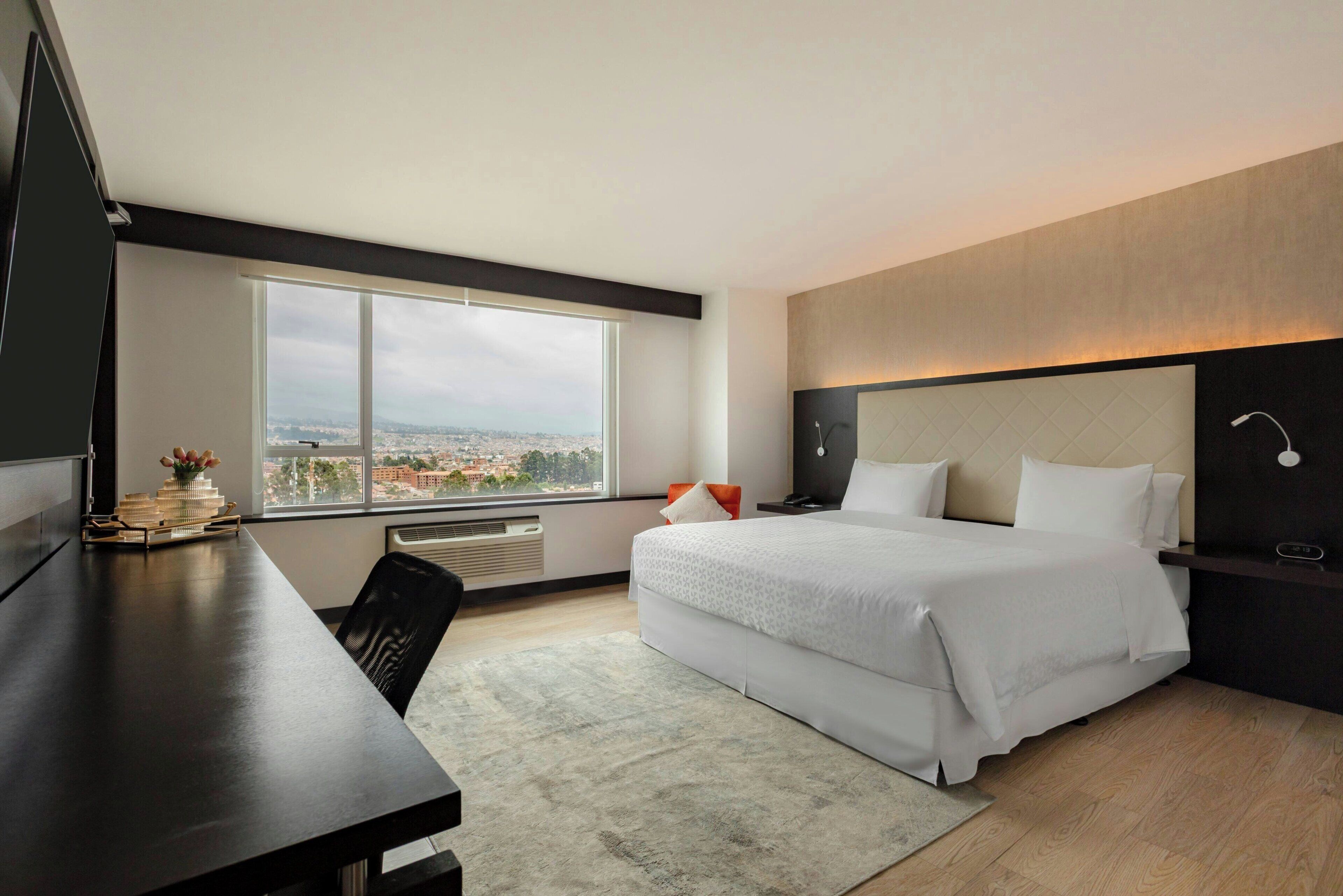 A modern hotel room with a large bed, a desk, and a view of the city.