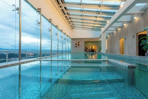Una piscina infinita con cerramiento de vidrio, vista a la ciudad, techo con tragaluces y diseño interior moderno.
