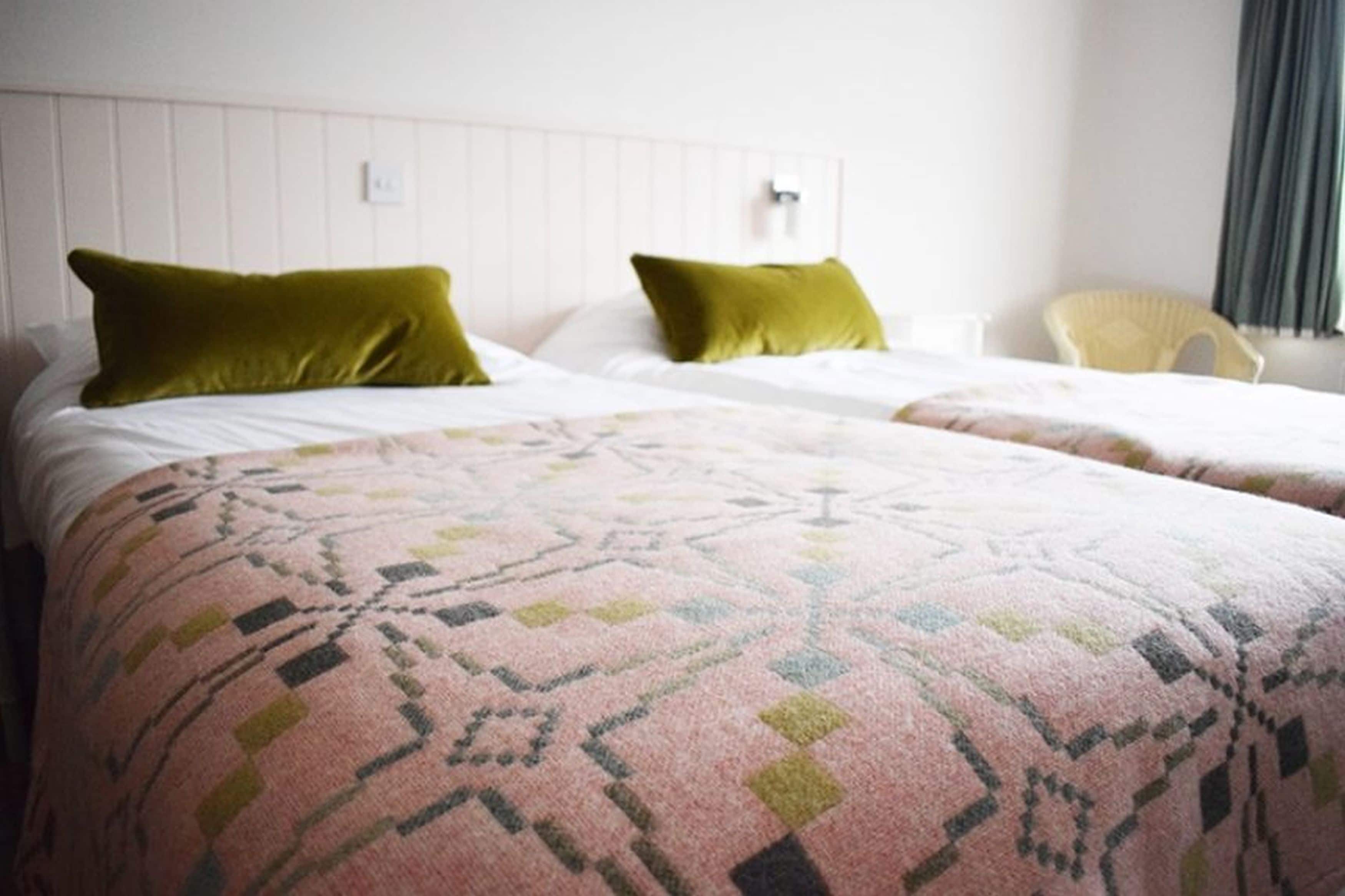 A hotel room with two beds, each with a green pillow and a patterned blanket.