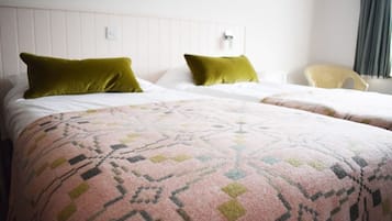 A hotel room with two beds, each with a green pillow and a patterned blanket.