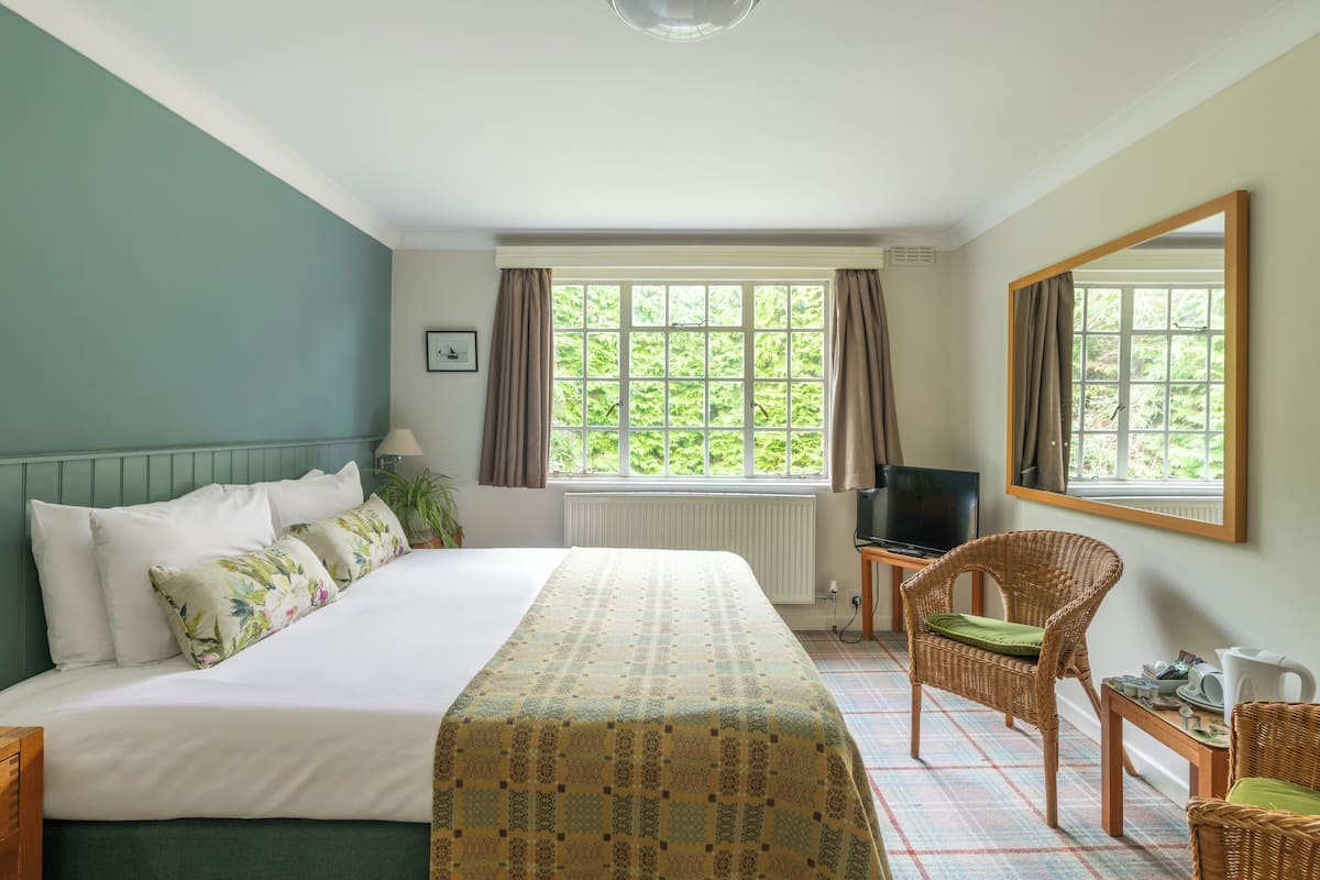 A hotel room with a bed, a television, a wicker chair, and a window with curtains.