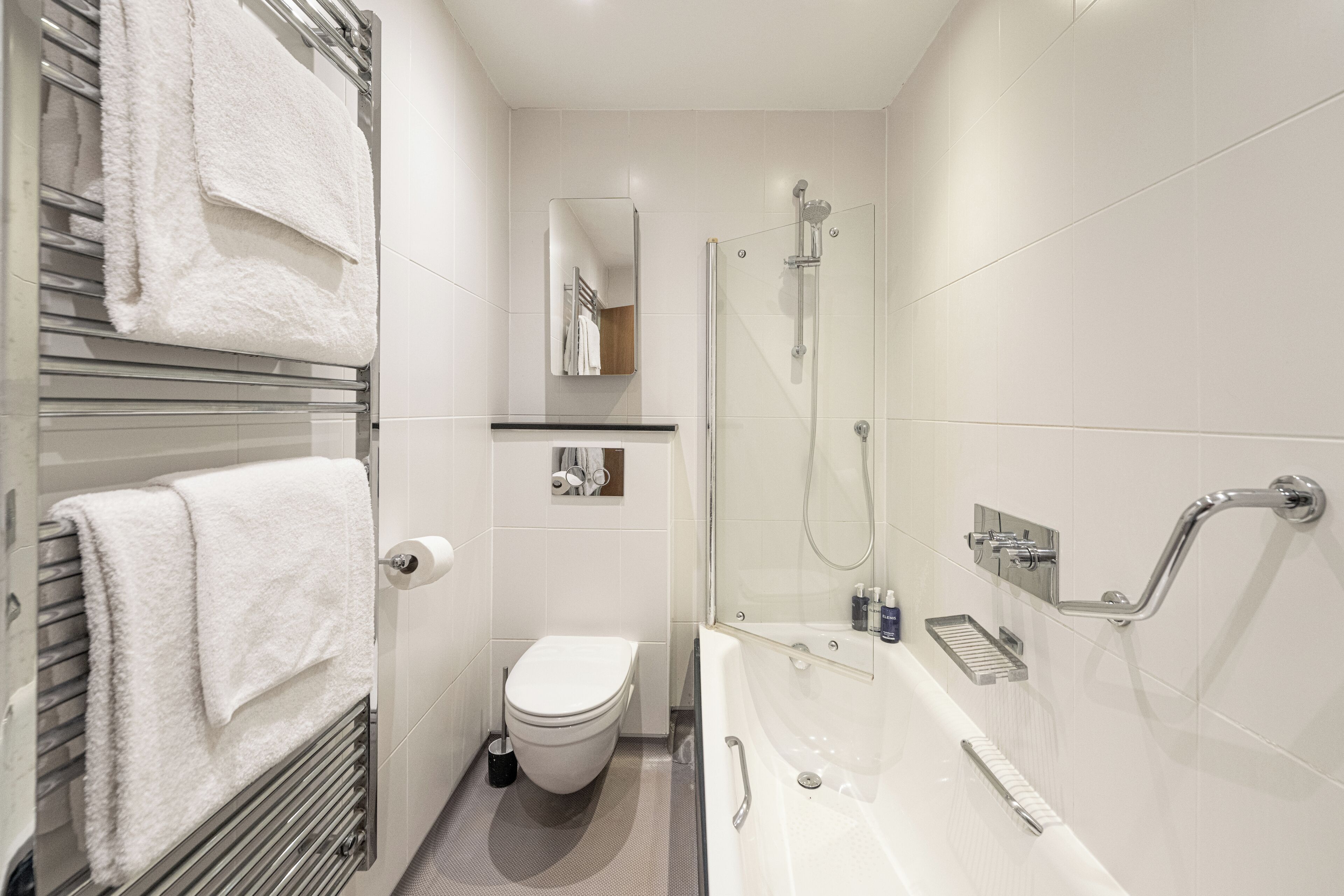A modern bathroom with a glass-enclosed shower, a white bathtub, and a toilet.