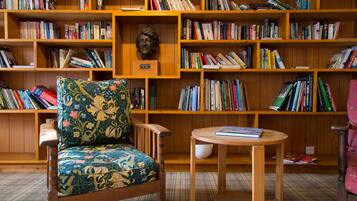Una biblioteca con estanterías de madera llenas de libros, un sillón con cojín floral y una pequeña mesa de madera.