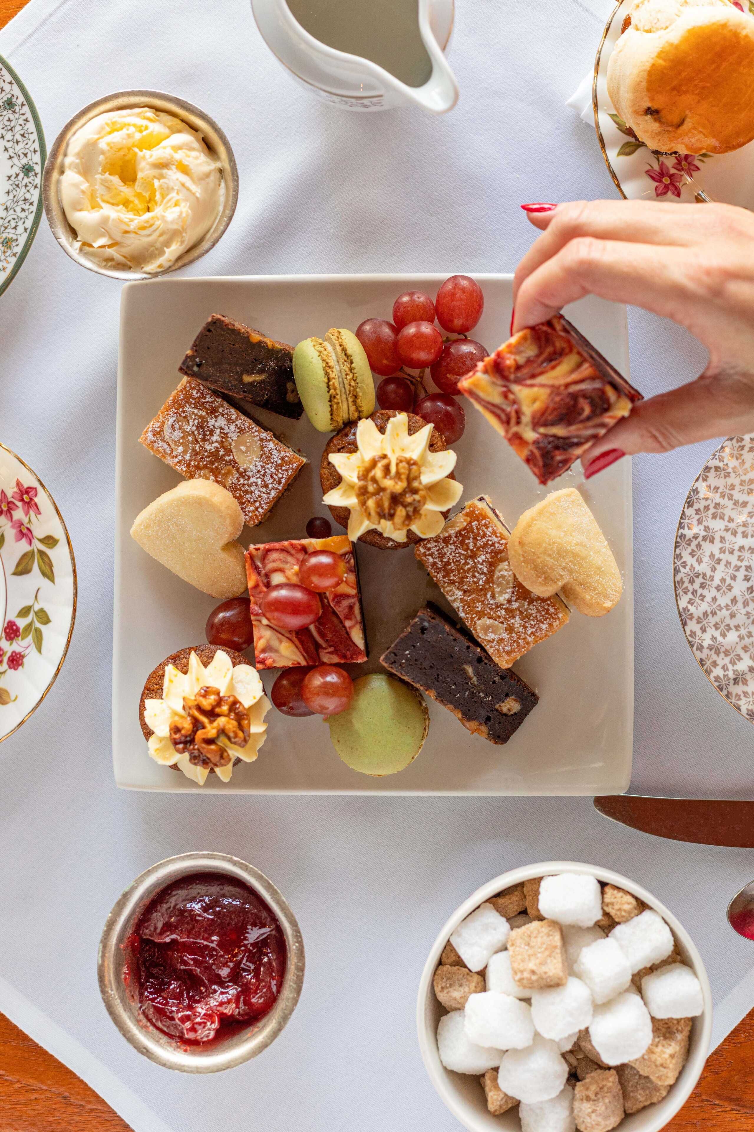 A tray of assorted desserts including cakes, macarons, and fruit, with a cup of coffee and a bowl of marshmallows.