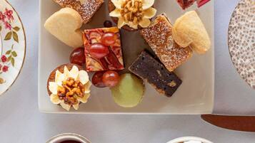 A tray of assorted desserts including cakes, macarons, and fruit, with a cup of coffee and a bowl of marshmallows.