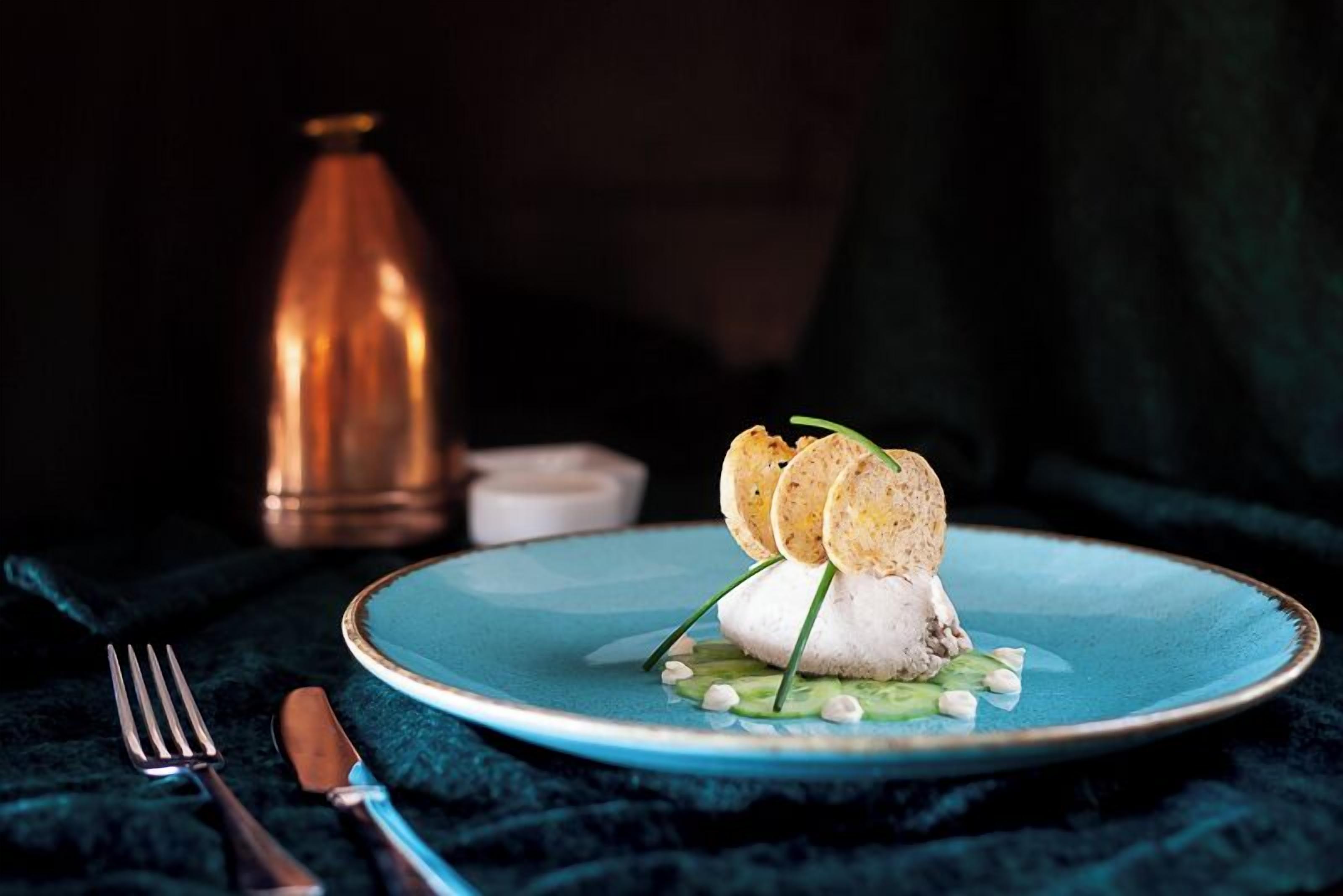 A plate with a white food item, green garnish, and two round, crispy elements on a blue plate.