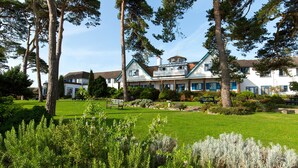 A large house with a balcony, surrounded by a well-maintained lawn and trees. - The Knoll House (Swanage)