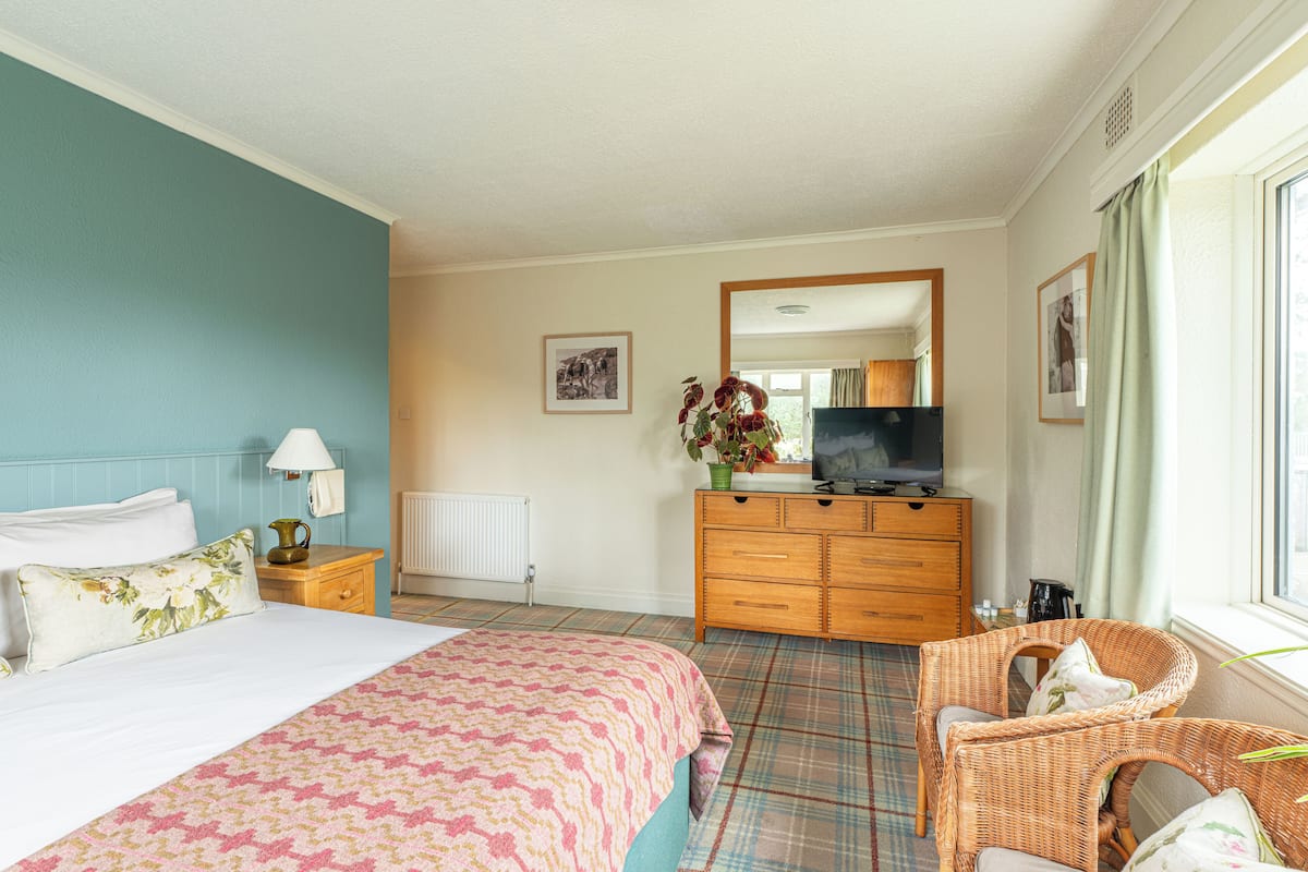 A hotel room with a bed, a dresser, a television, and a wicker chair.