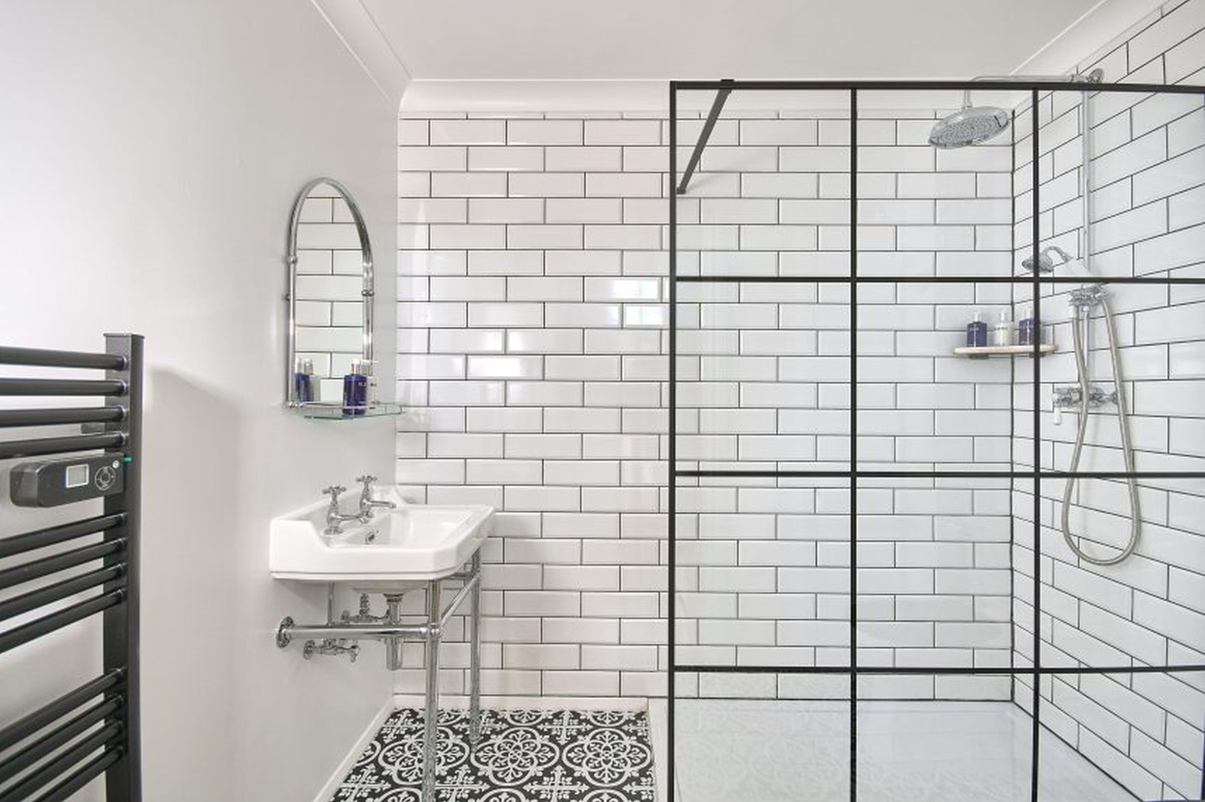 A bathroom with white subway tiles, a white sink, a mirror, and a shower with a glass door.