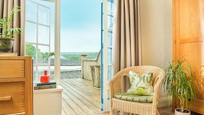 A room with a wicker chair, a potted plant, a wooden cabinet, and a view of a balcony with a railing. - The Knoll House (Swanage)