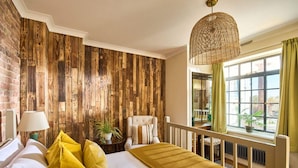 A bedroom with a wooden wall, a bed with yellow pillows, a hanging light fixture, and a view of the outdoors through a window. - The Knoll House (Swanage)