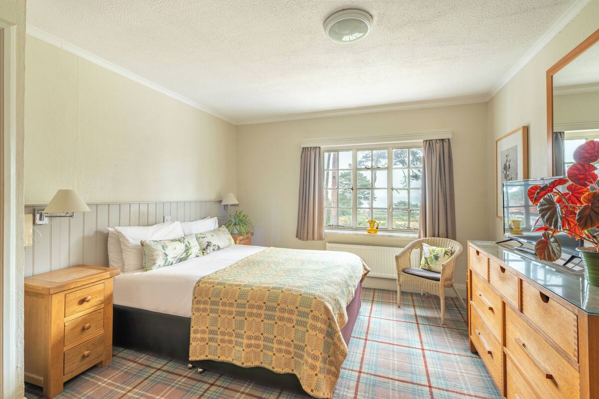 A bedroom with a bed, a dresser, a chair, a window with curtains, and a radiator.