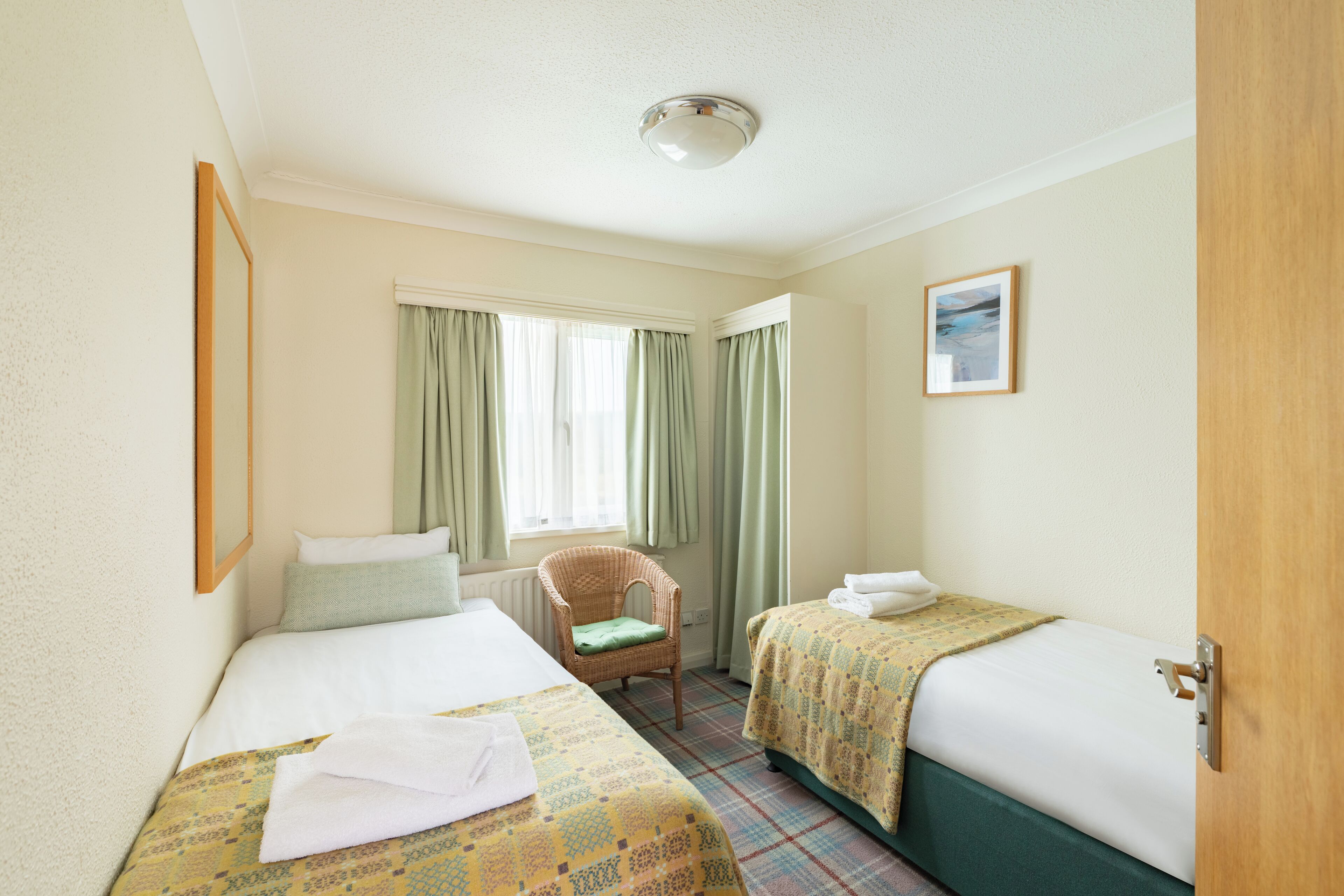 A hotel room with two beds, a chair, a window with curtains, and a picture on the wall.