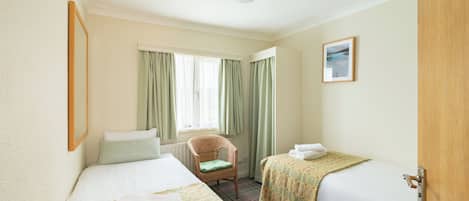 A hotel room with two beds, a chair, a window with curtains, and a picture on the wall.