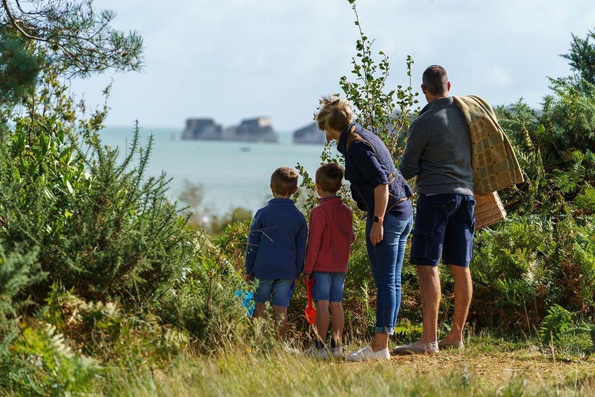 A family standing on a grassy area with a view of the sea and distant islands.