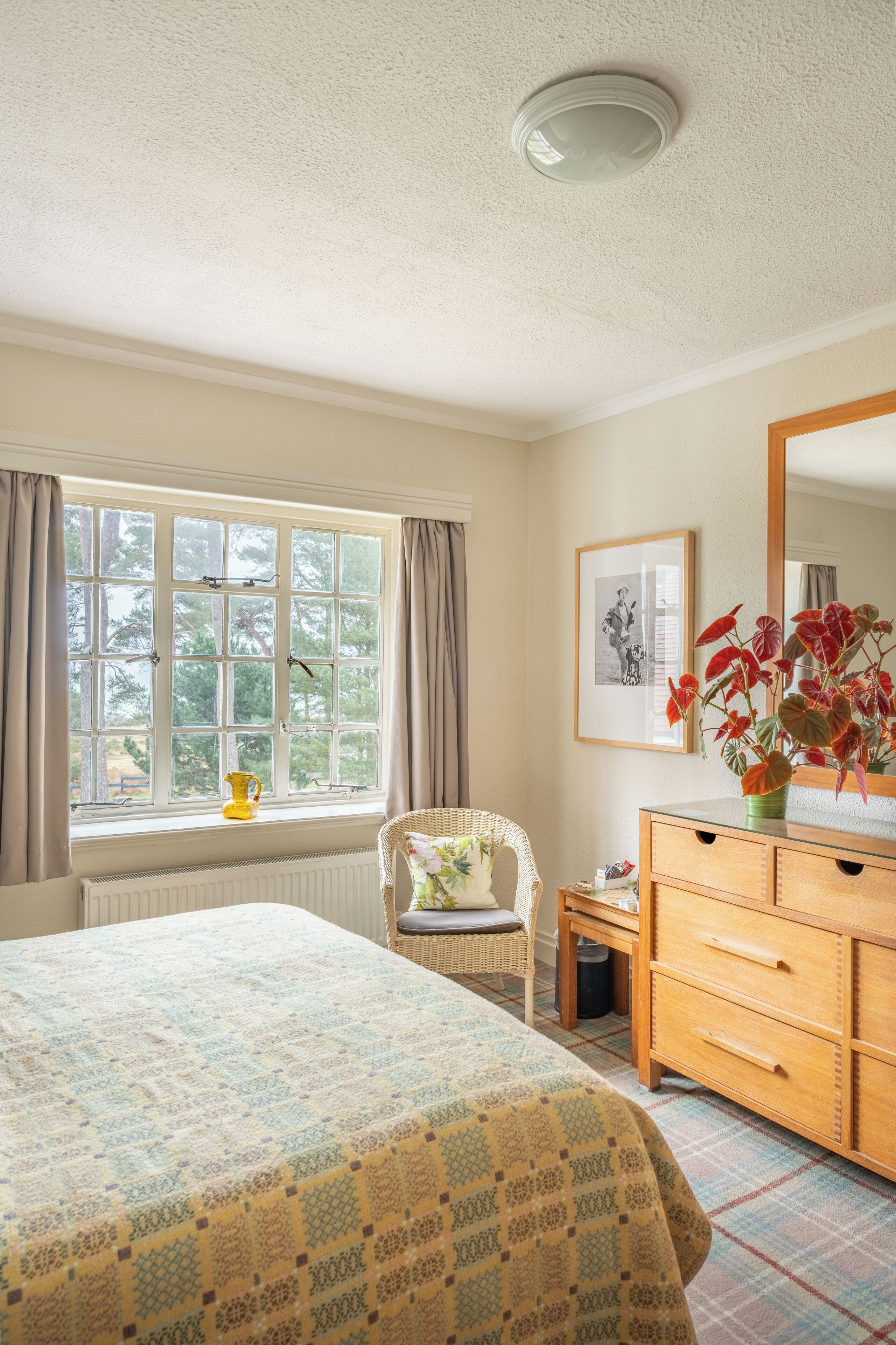 A bedroom with a bed, a chair, a dresser, a window with curtains, and a framed picture on the wall.