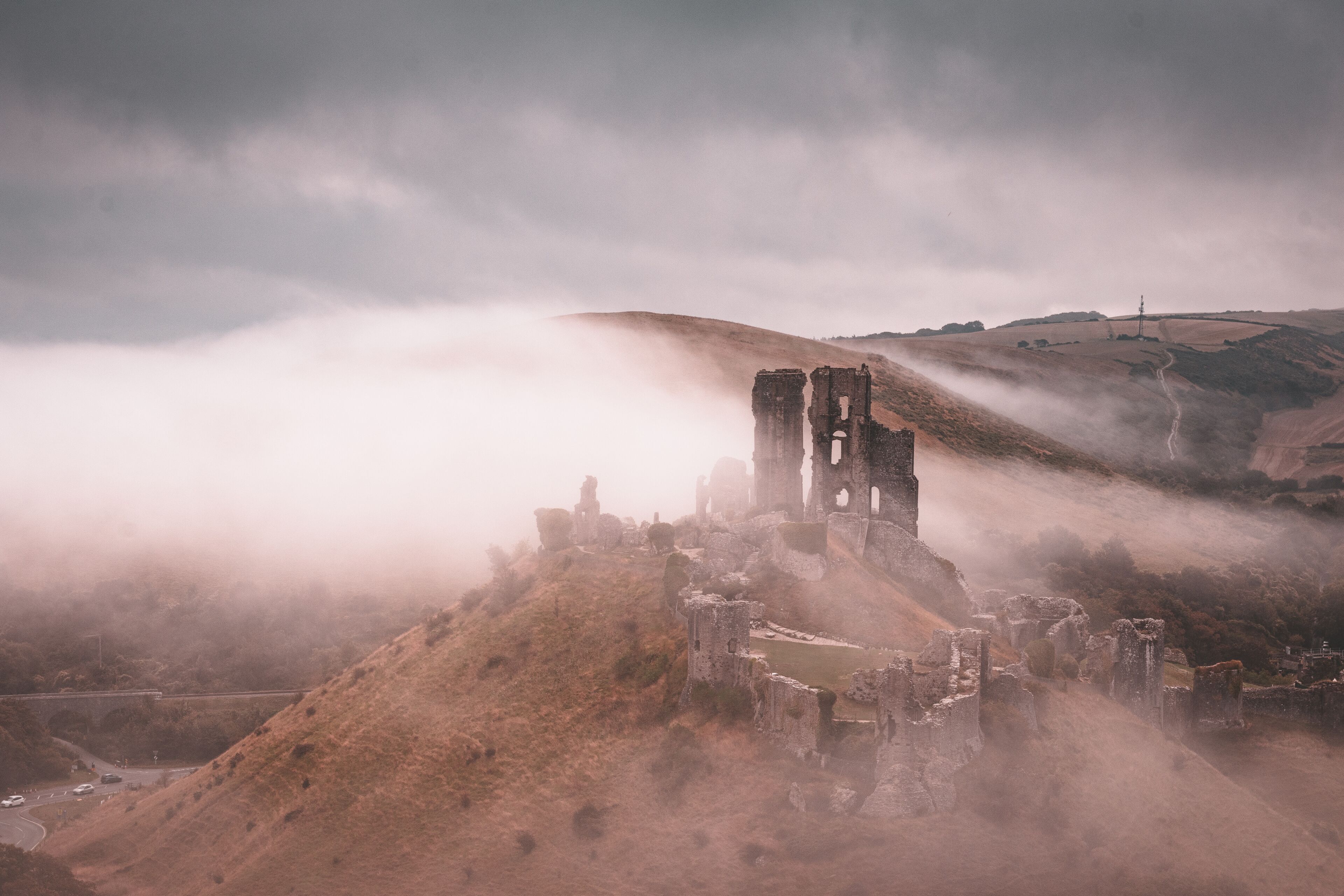 A historic stone structure with ruins, surrounded by mist and hills.
