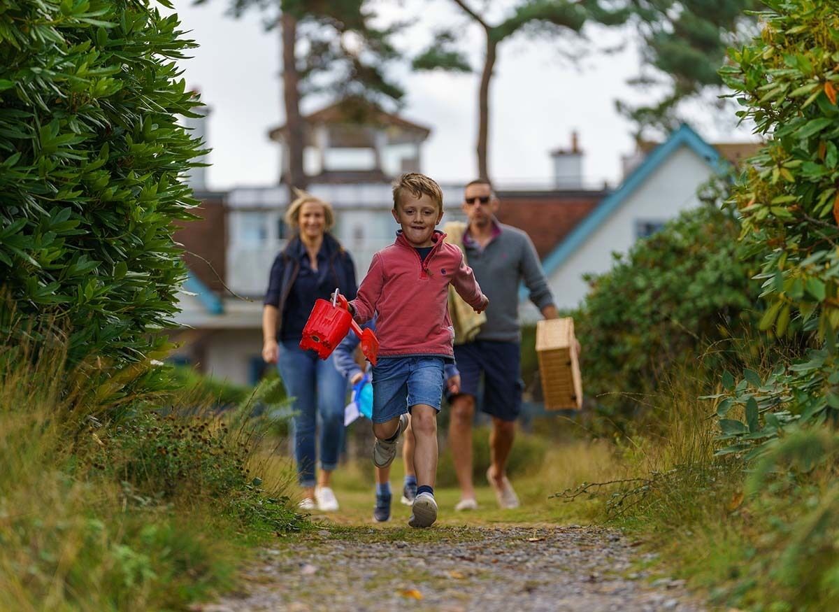Un chemin bordé de verdure des deux côtés, menant à un bâtiment surmonté d’un toit bleu.