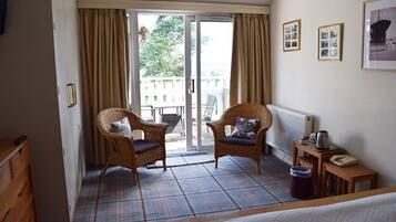 Ett hotellrum med ett rutigt golv, två flätade fåtöljer, ett litet bord med en vattenkokare, ett element och utsikt genom en skjutdörr.